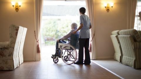 Care worker stands behind a care home resident in a wheelchair