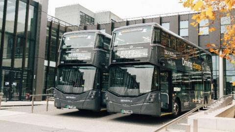 Black double-decker buses with "switch to electric" on the departure boards
