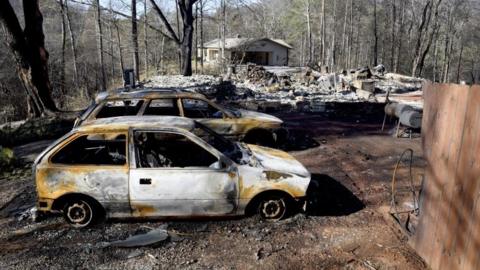 Charred home and cars sit on a property, while a neighbour's home, background, is undamaged Thursday, in Gatlinburg