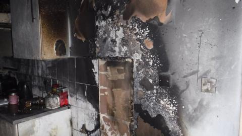 A wall and cupboards blackened by smoke in a kitchen