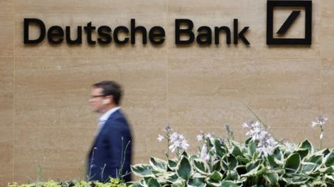 A pedestrian walks past a logo outside the offices of German bank Deutsche Bank in central London on July 8, 2019.