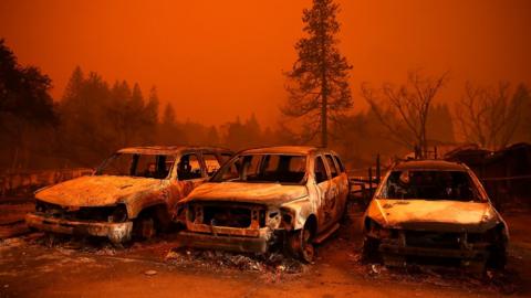 Cars destroyed by Camp Fire sit burned out in front of orange skyline