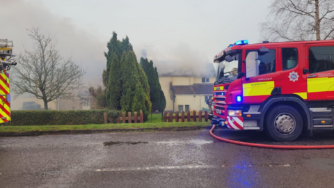 Fire engine on road near house damaged by fire