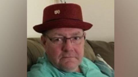 Gary Piatek, a white, middle-aged man wearing a red hat and mint green polo shirt. 