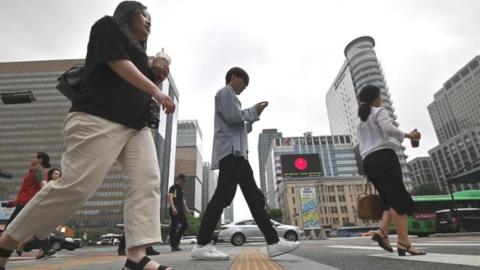 People walk cross a road at a business district in Seoul
