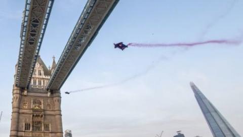 Marco Furst and Marco Waltenspiel fly under the top section of Tower Bridge in London in their wingsuits, leaving behind red smoke trails