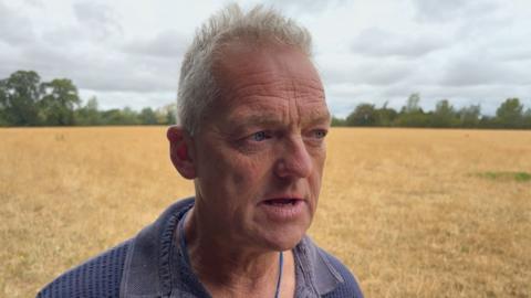 Headshot of a man in a field of ploughed crop - yellow stalks remain.