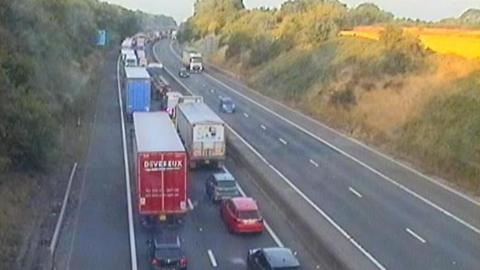 A motorway camera image showing a long queue of vehicles on the carriageway to the left, with three vehicles travelling on the right side of the carriageway
