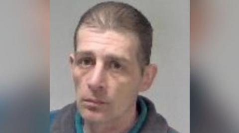 Paul Davies is seen in a police mugshot. He has short, thinning brown hair and lines on his forehead. He is wearing a blue and grey fleece over a grey top.