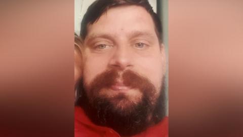 A close-up picture of a man with a red top. He is looking at the camera