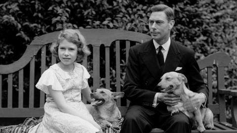 July 1936: George, Duke of York and Princess Elizabeth sitting on a bench with their corgi dogs in the grounds of their London home, 145 Piccadilly.