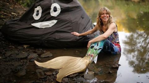 Lindsey Cole wearing a mermaid's tail sitting by a river