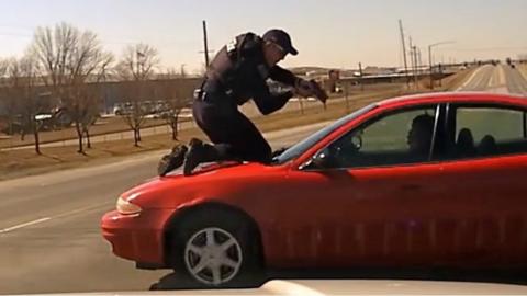 Officer on car bonnet pointing gun at passenger