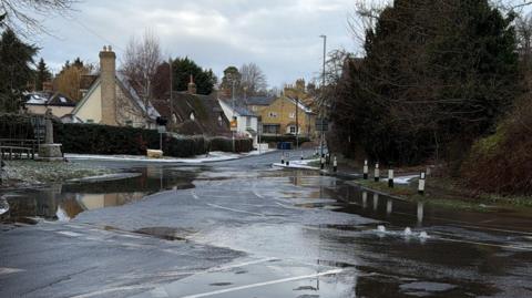 Picture of the street. Water can be seen flowing out onto the ground with cottages in the background.
