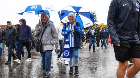 Two women walking in the rain with umbrellas at the Amex stadium in Brighton