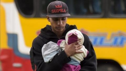 A Venezuelan migrant carries a baby at an improvised camp near a bus terminal in Bogota on September 11, 2018.