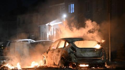 An upturned car burns amid disorder in the Cardiff district of Ely