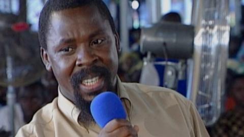 TB Joshua holding a blue microphone