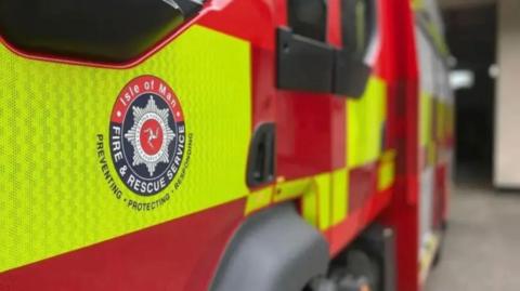 The Isle of Man Fire and Rescue Service blue and white emblem on the door of a parked fire engine.