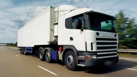 A white HGV lorry on a dual carriageway. Blurred trees in the background