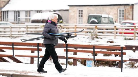 A woman walks through snow with a pair of skis in Carrbridge in the Scottish Highlands