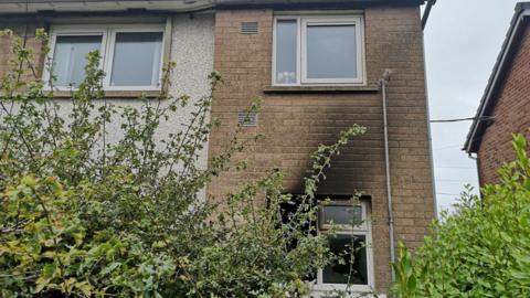 the front of a semi-detached or end-terrace house, showing blackened bricks on part of the wall