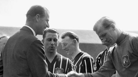 The Duke of Edinburgh smiles while shaking hands with Manchester City"s Footballer of the Year Bert Trautmann, before the FA Cup final at Wembley