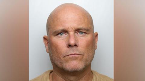 Mugshot of Richard Whitaker, who has a bald head, stubble and is wearing a yellow jumper.