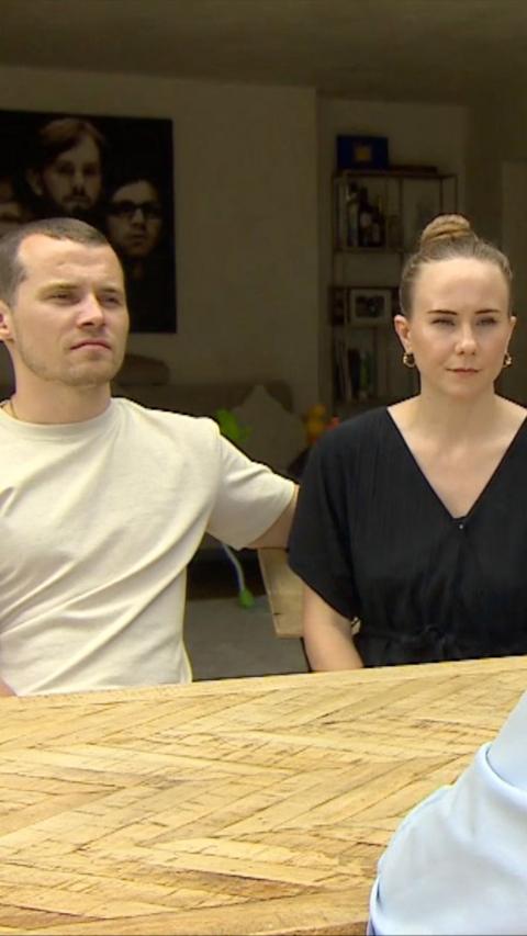Young man wearing white t-shirt sat next to young woman in a black top sat around a wooden table indoors