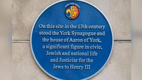 An image of the blue plaque which reads: 'On this site in the 13th century stood the York Synagogue and the house of Aaron of York, a significant figure in civic, Jewish and national life and Justiciar for the Jews to Henry III.