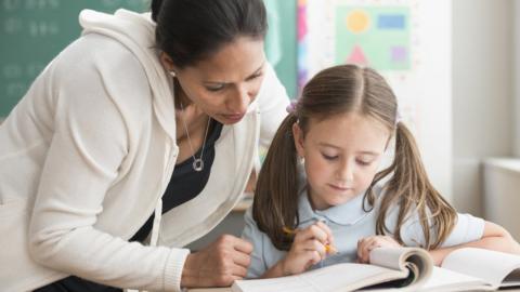 Teacher helping pupil in classroom (stock photo)