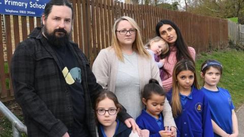Parents stand with their children outside Great Gidding School Cambridgeshire