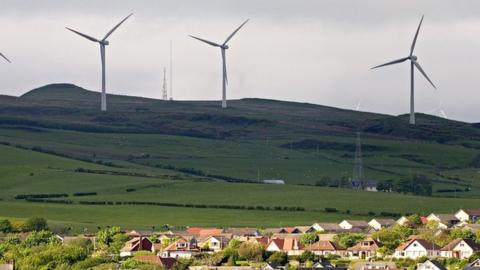 Wind turbines in back ground, and housing estate on edge of field by sea in forehround