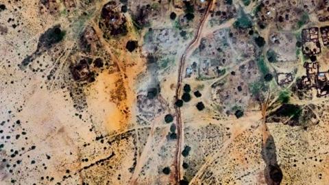 A satellite image of Alsen village near el-Fasher taken on 25 July 2025 showing the outline of the various houses and trees with a line showing the earthen wall weaving through the settlement.