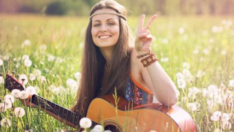 A young woman makes a peace symbol with her fingers while walking through a meadow