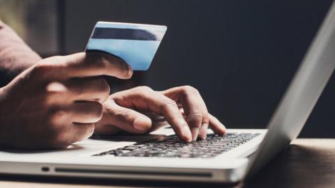 A woman holding a credit card and typing on a laptop keyboard