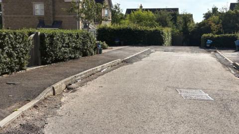 A road at a housing estate has uneven pavements.