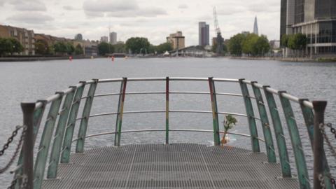 A dockland area with housing and boats at the quayside with flowers tied to the railing. 