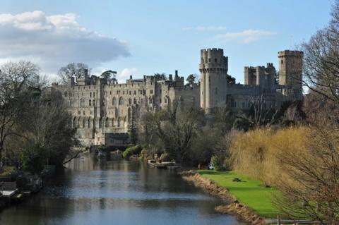 An image of Warwick's grey stone medieval castle taken from a bridge over the river Avon