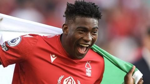 Taiwo Awoniyi in Nottingham Forest kit smiles and celebrates with Nigerian flag over shoulders