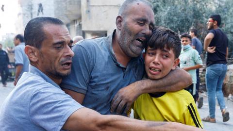 A Palestinian man wounded in an Israeli strike is helped by a boy in Rafah, in the southern Gaza Strip (17 October 2023)