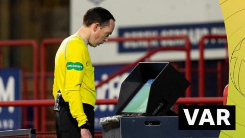 Referee Colin Steven reviews the action on the pitchside monitor