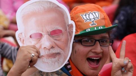 An Indian woman holds Prime Minister Narendra Modi mask cheers as she attends his election campaign rally at Kathua, about 90kms from Jammu,