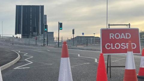 Road closure signs and cones with the Herring Bridge in the raised position in the background