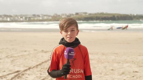 Child Max looking at camera stood on a beach.