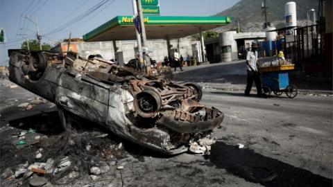 A man pulls a cart as he walks past a burnt car on a street of Port-au-Prince, Haiti, July 8, 2018.