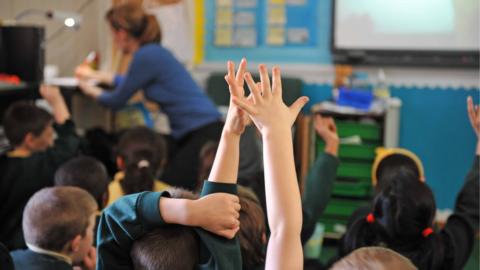 Children raise hands in classroom