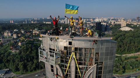 People on top of the statue with a Ukrainian flag