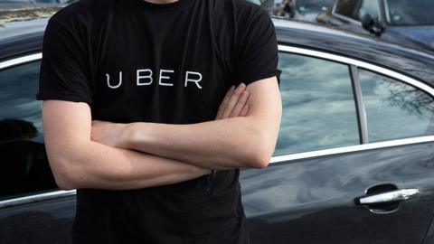 A man wearing an Uber t-shirt and standing in front of a car