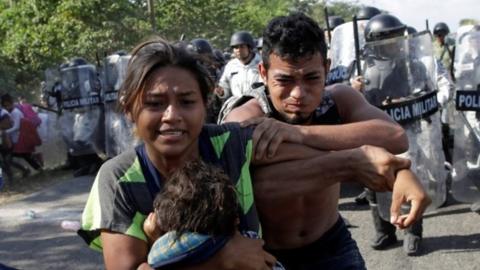 Migrants, mainly from Central America, react as members of the security forces approach to them
